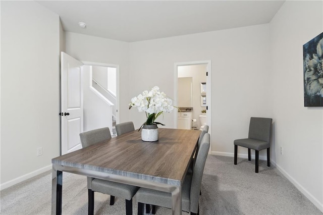 dining space with light colored carpet, baseboards, and stairs