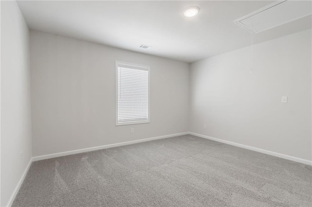 carpeted spare room featuring baseboards, visible vents, and attic access