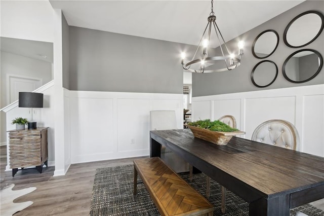 dining area with wood finished floors, an inviting chandelier, a wainscoted wall, and a decorative wall