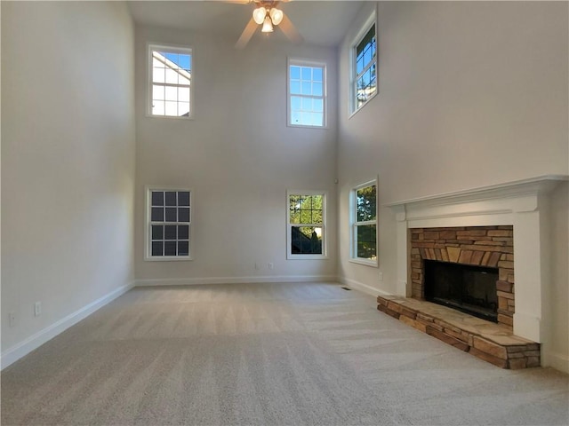 unfurnished living room featuring light colored carpet, a fireplace, a towering ceiling, and a healthy amount of sunlight