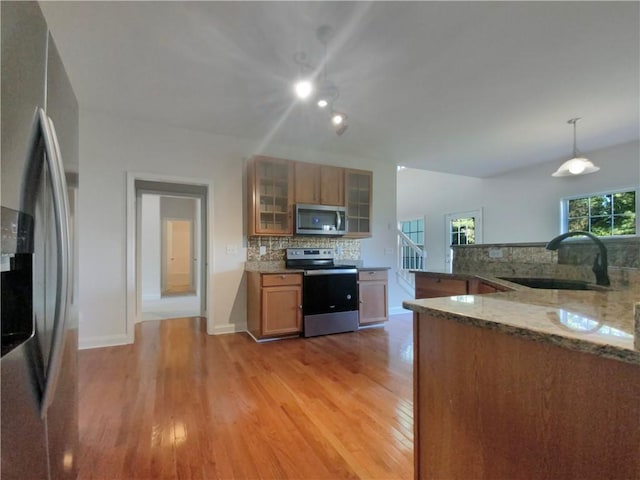 kitchen featuring hanging light fixtures, sink, tasteful backsplash, light hardwood / wood-style flooring, and stainless steel appliances