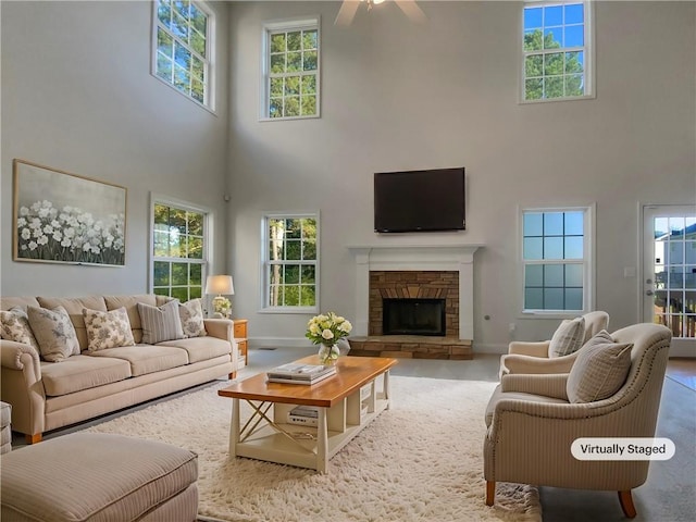 living room with ceiling fan, a high ceiling, a wealth of natural light, and a stone fireplace