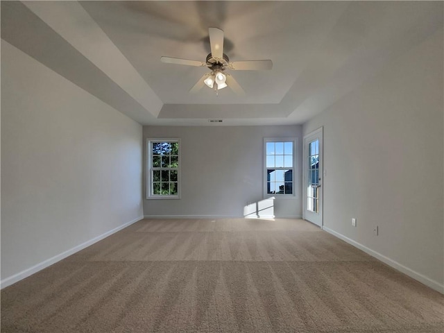 carpeted empty room with a healthy amount of sunlight, ceiling fan, and a raised ceiling