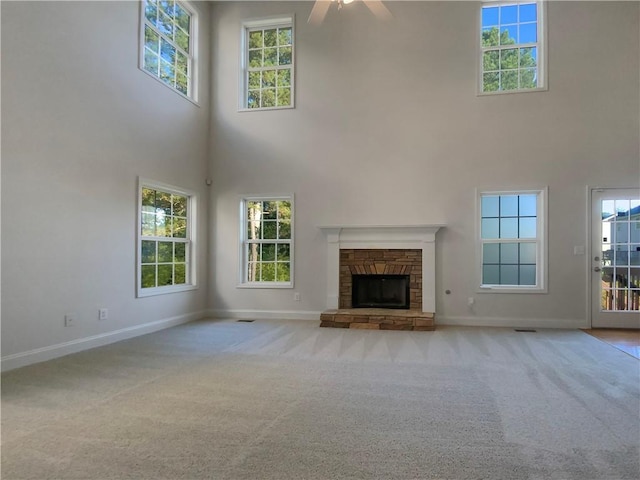 unfurnished living room with a healthy amount of sunlight, ceiling fan, a towering ceiling, and light colored carpet