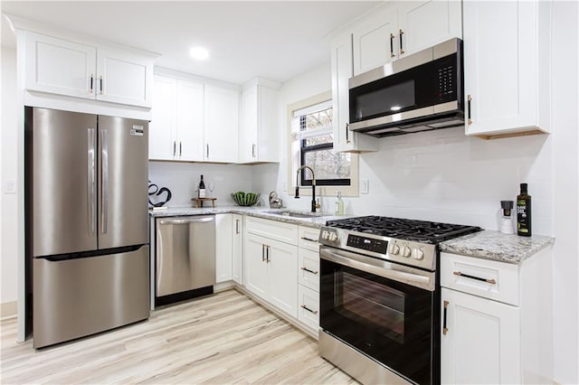 kitchen with white cabinets, stainless steel appliances, light wood-style flooring, and a sink