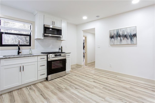 kitchen featuring light stone counters, light wood finished floors, a sink, white cabinets, and appliances with stainless steel finishes