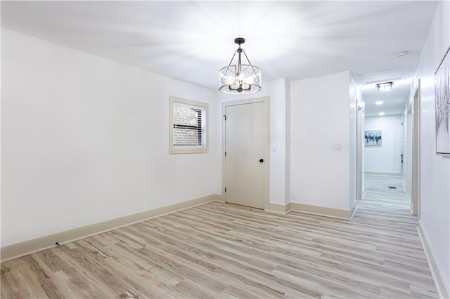 unfurnished room with baseboards, light wood-type flooring, and a chandelier