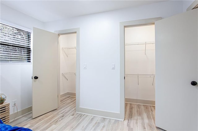 unfurnished bedroom featuring a spacious closet, light wood-style floors, and a closet