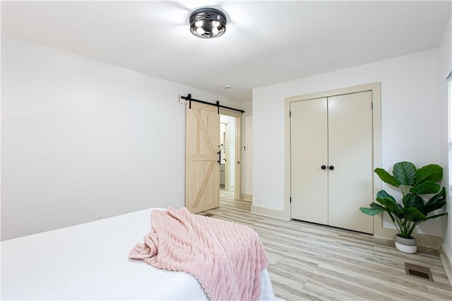 bedroom with light wood finished floors, visible vents, baseboards, a barn door, and a closet