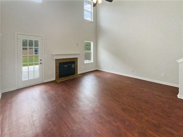 unfurnished living room with dark hardwood / wood-style flooring, a high ceiling, a high end fireplace, and ceiling fan