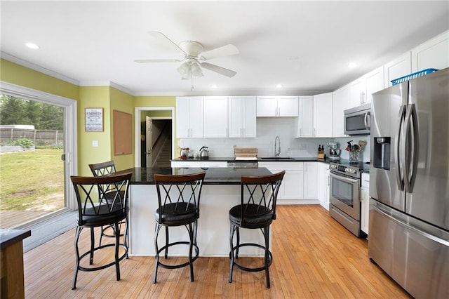 kitchen with a kitchen island, a kitchen bar, appliances with stainless steel finishes, a sink, and white cabinets