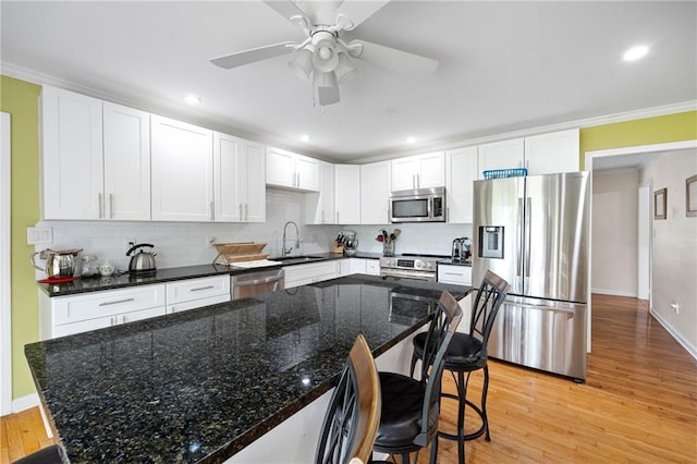 kitchen with decorative backsplash, a breakfast bar, a sink, light wood finished floors, and appliances with stainless steel finishes