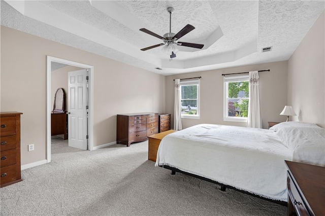 carpeted bedroom featuring baseboards, a textured ceiling, visible vents, and a tray ceiling