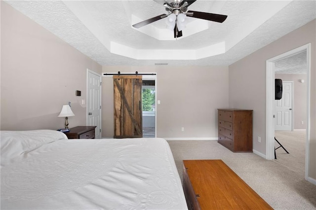 bedroom with a textured ceiling, a barn door, baseboards, a raised ceiling, and carpet flooring