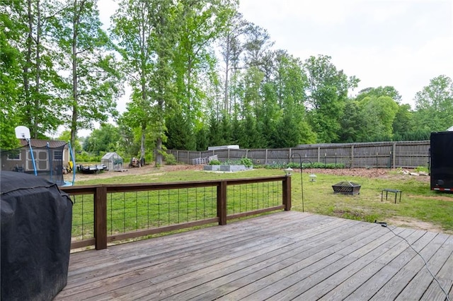 wooden deck featuring a lawn, a storage shed, a fenced backyard, an outdoor fire pit, and a grill