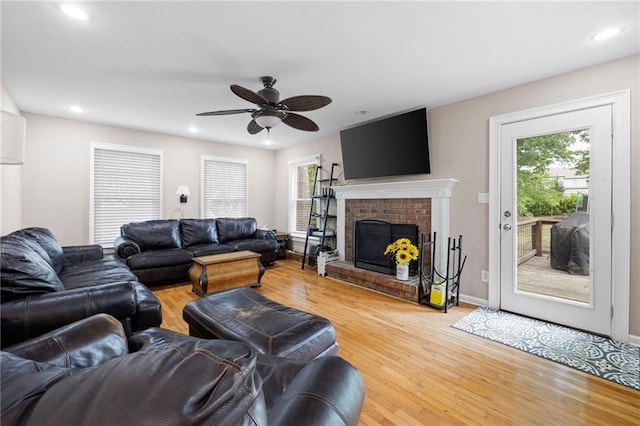 living room with light wood-type flooring, a ceiling fan, a wealth of natural light, and a fireplace
