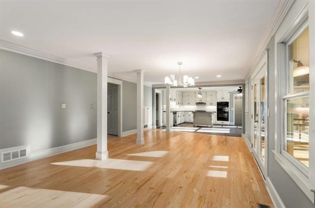 unfurnished living room featuring ornamental molding, ornate columns, an inviting chandelier, and light hardwood / wood-style floors