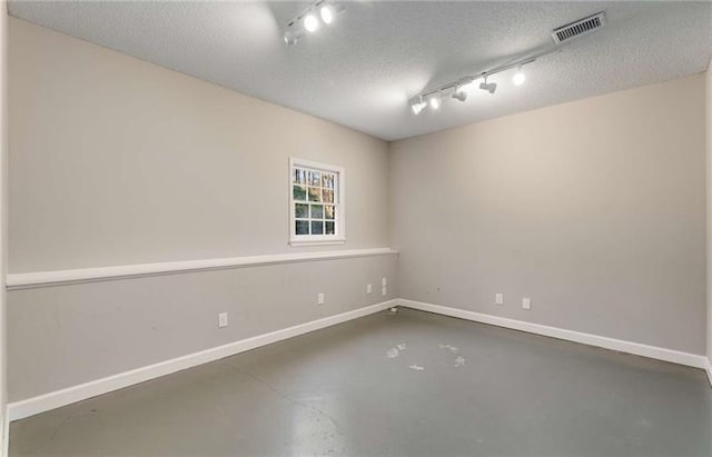 empty room with concrete flooring, a textured ceiling, and rail lighting