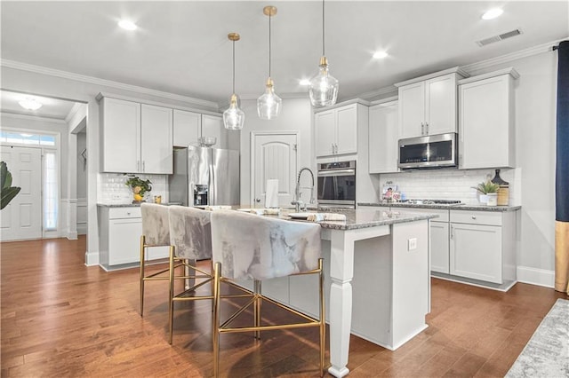 kitchen with stainless steel appliances, white cabinets, and an island with sink