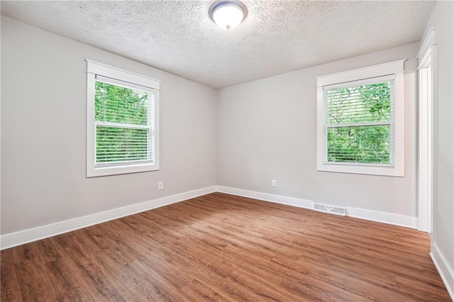 empty room with wood finished floors, a textured ceiling, and baseboards