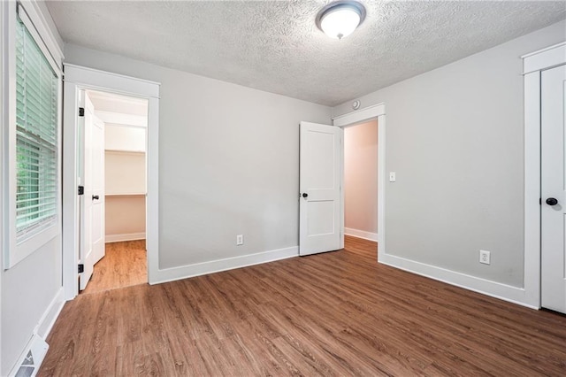 unfurnished bedroom with a closet, wood finished floors, a textured ceiling, and baseboards