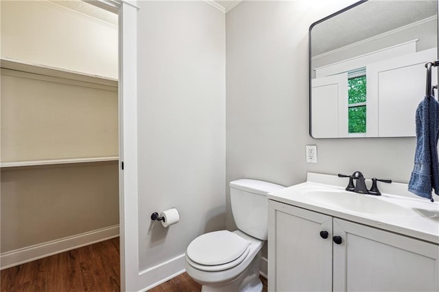 half bath with ornamental molding, wood finished floors, toilet, vanity, and baseboards