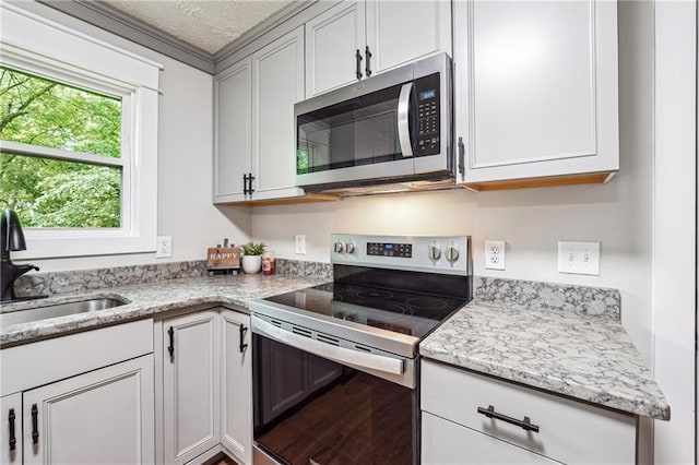 kitchen with appliances with stainless steel finishes, a sink, light stone counters, white cabinets, and a textured ceiling