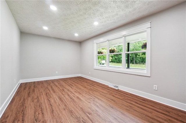 empty room featuring recessed lighting, wood finished floors, a textured ceiling, and baseboards