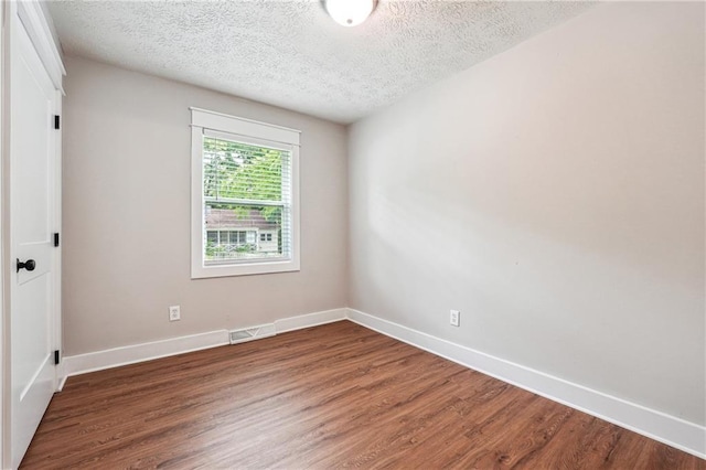 empty room featuring a textured ceiling, wood finished floors, and baseboards