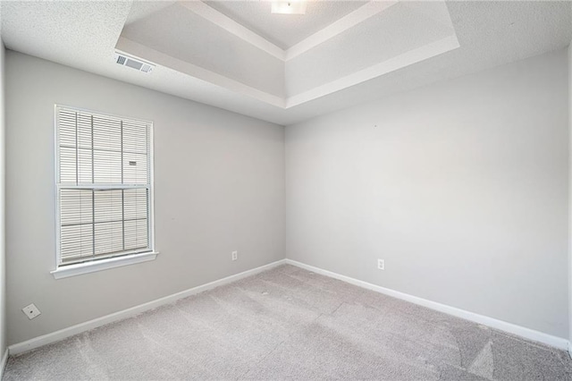 empty room with a raised ceiling, light carpet, visible vents, and a textured ceiling