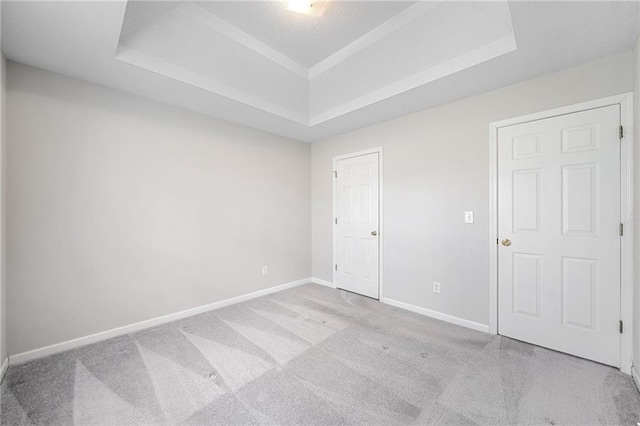 empty room with a textured ceiling, carpet floors, a raised ceiling, and baseboards