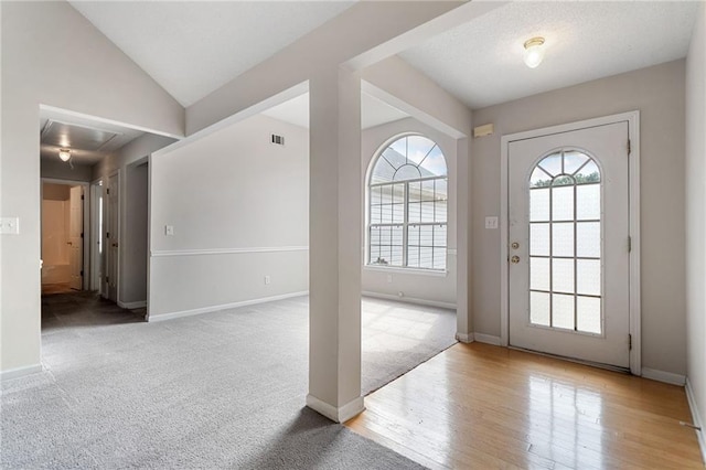 carpeted foyer entrance with lofted ceiling, wood finished floors, visible vents, and baseboards