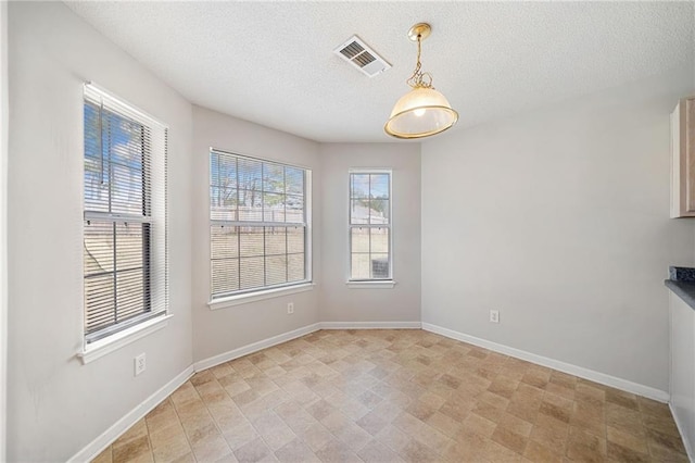 unfurnished dining area featuring visible vents, a textured ceiling, and baseboards