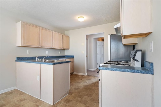 kitchen with range with gas stovetop, dark countertops, a peninsula, light brown cabinets, and a sink