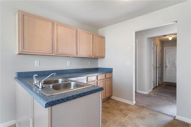 kitchen featuring dark countertops, light brown cabinets, a sink, and a peninsula