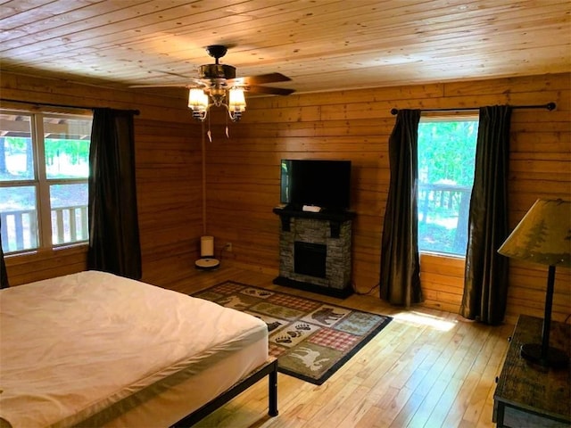 bedroom featuring a stone fireplace, wooden ceiling, wood walls, and light wood-type flooring