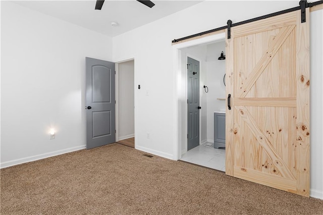 unfurnished bedroom with a barn door, ensuite bath, carpet floors, baseboards, and visible vents
