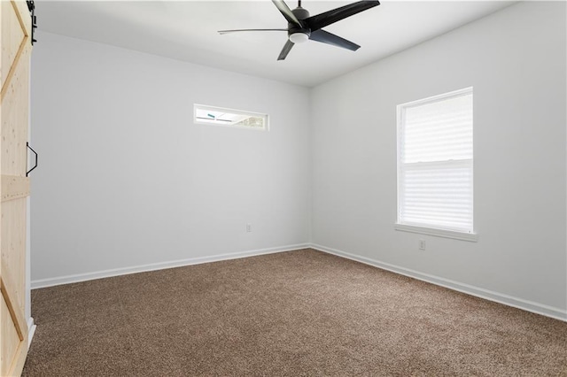 empty room featuring baseboards, ceiling fan, carpet, and a barn door