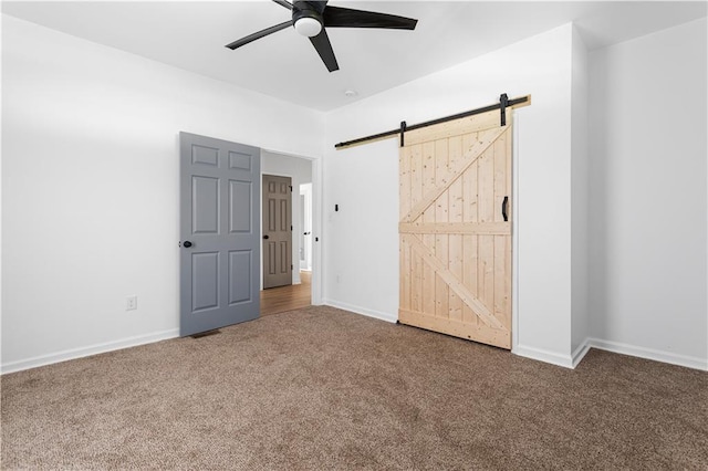 unfurnished bedroom with carpet floors, a barn door, baseboards, and a ceiling fan