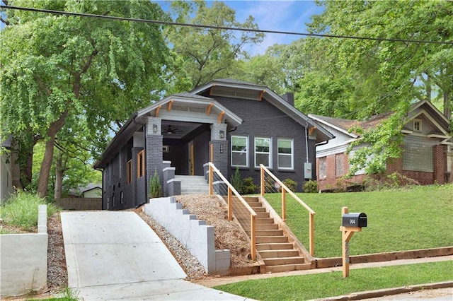 view of front of property with ceiling fan, driveway, brick siding, a front lawn, and stairs