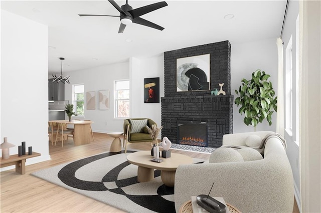 living room with baseboards, ceiling fan, a brick fireplace, and wood finished floors
