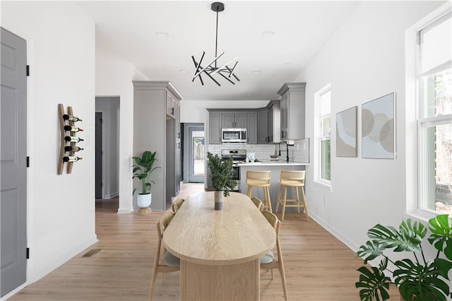 dining room with plenty of natural light, light wood finished floors, and a notable chandelier