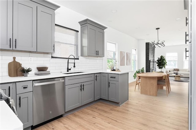 kitchen featuring tasteful backsplash, stainless steel dishwasher, gray cabinetry, a sink, and light wood-style flooring