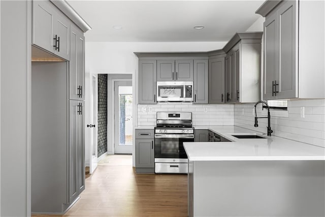 kitchen featuring gray cabinetry, appliances with stainless steel finishes, backsplash, and a sink
