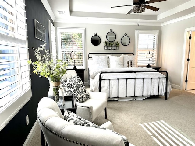 carpeted bedroom with a tray ceiling, multiple windows, and ceiling fan