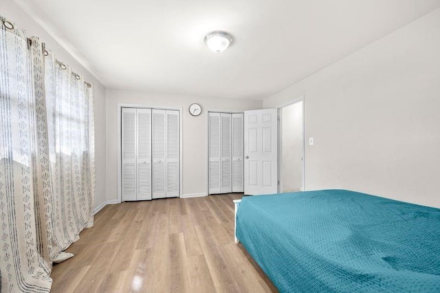 bedroom featuring baseboards, wood finished floors, and multiple closets