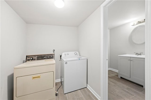 washroom with laundry area, separate washer and dryer, wood finish floors, a sink, and baseboards