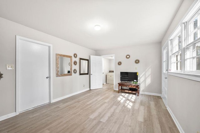 unfurnished living room featuring light wood-type flooring, washer / dryer, and baseboards