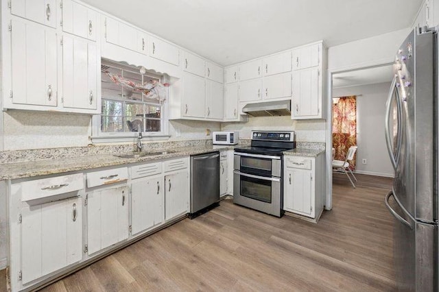 kitchen with under cabinet range hood, stainless steel appliances, a sink, light wood-style floors, and white cabinets