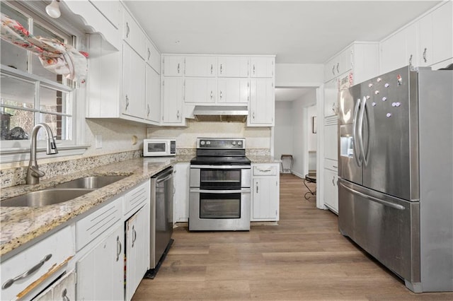 kitchen with range hood, appliances with stainless steel finishes, white cabinets, a sink, and light wood-type flooring